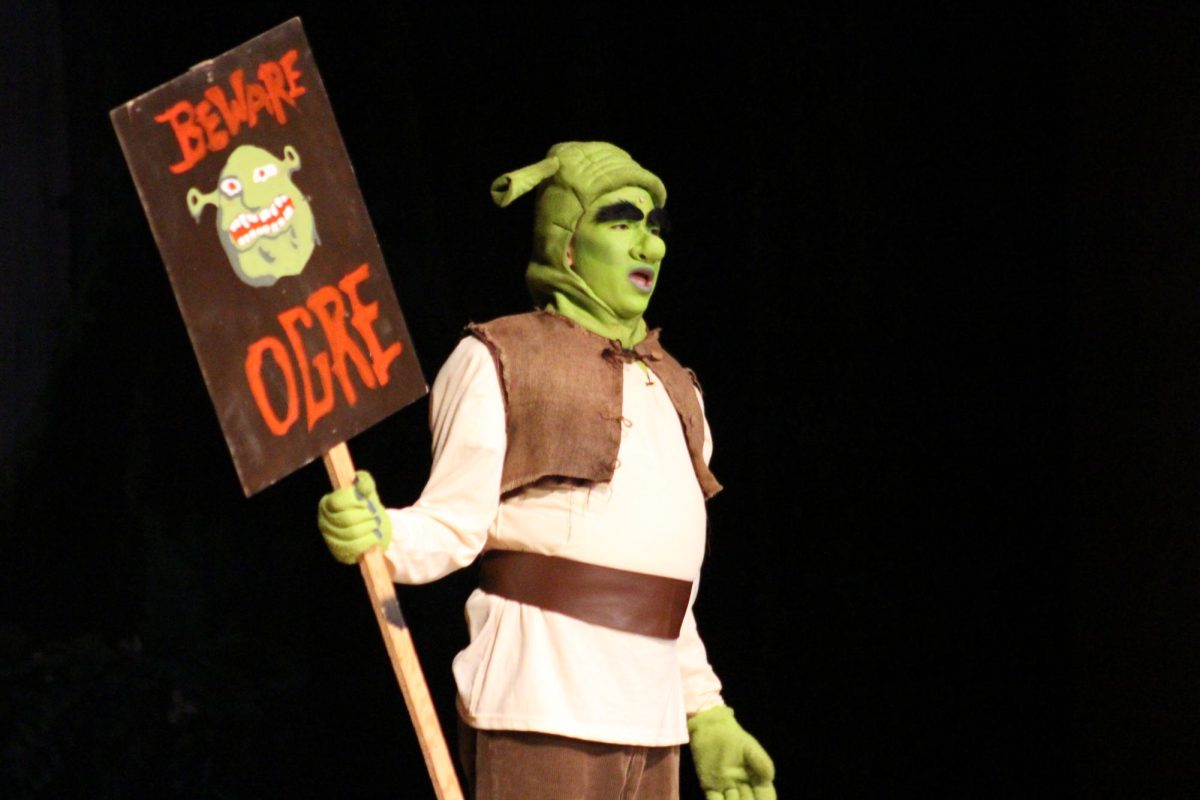 Colby Tong performs as Shrek, holding a “Beware Ogre” sign during the production of Shrek the Musical, March 20, 2026.
